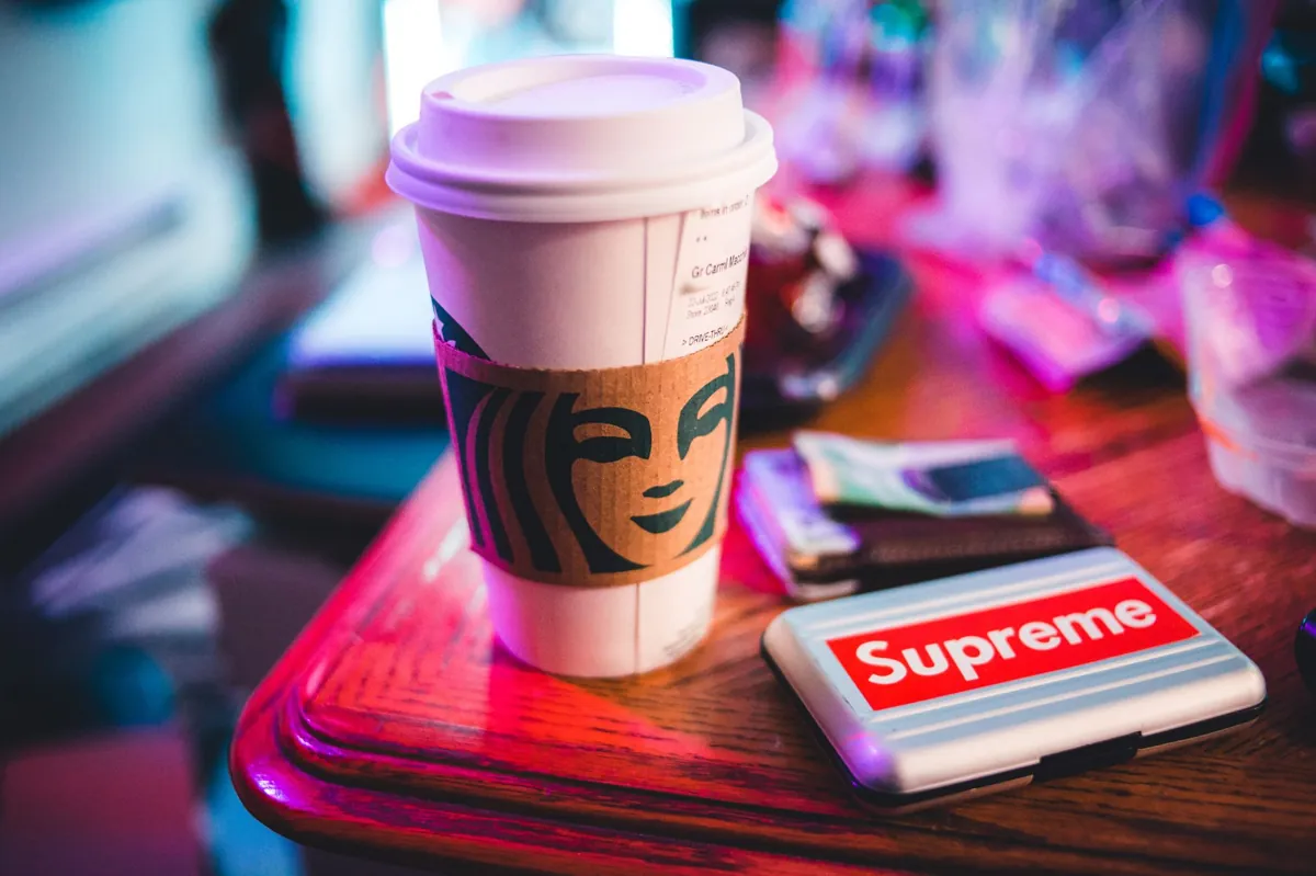 A coffee cup and Supreme logo on a wooden surface with vibrant lighting.