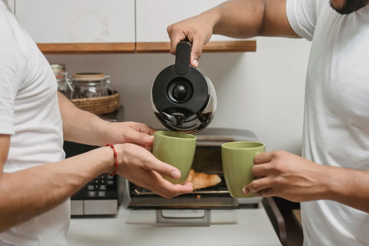 Two adults sharing a warm moment pouring coffee in a cozy kitchen.