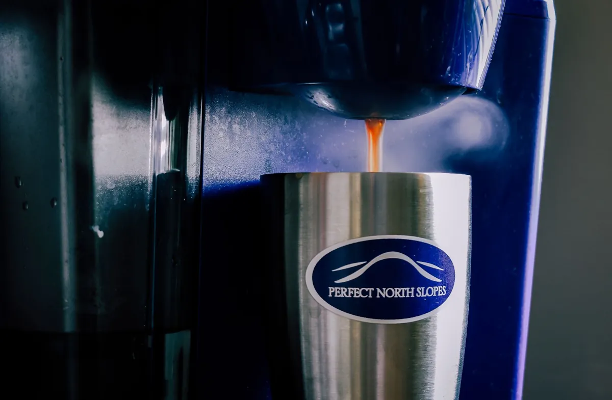 Stainless steel cup with coffee pouring from a coffee machine indoors.