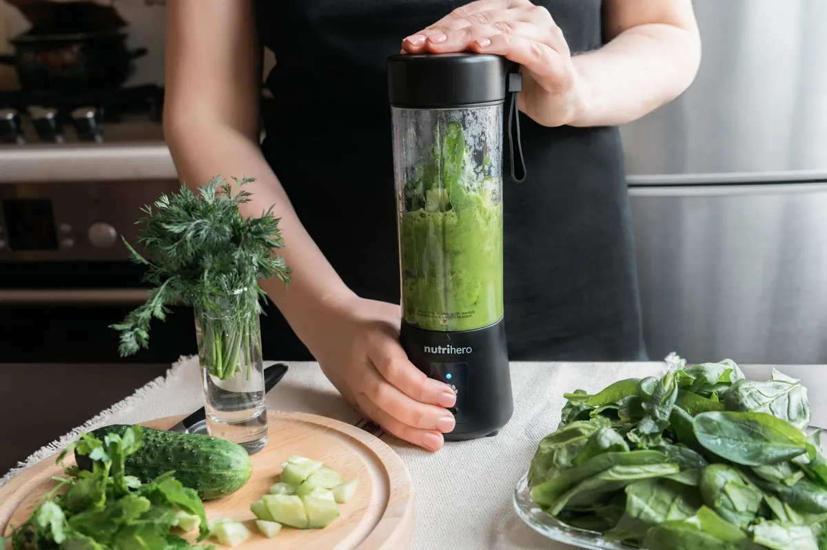 A person making a healthy green smoothie with fresh vegetables in a modern kitchen.