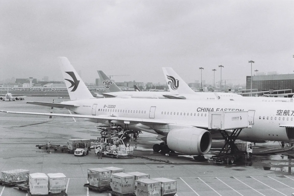 Black and white photograph of airplanes parked at an airport tarmac on a cloudy day.