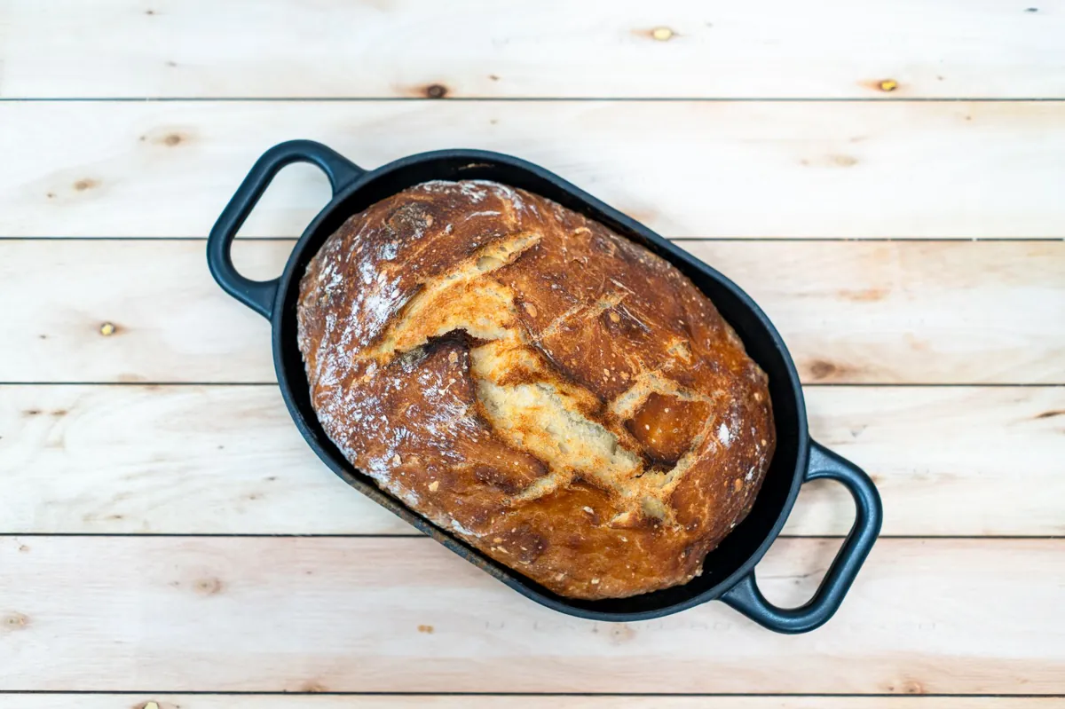 Top view of a homemade sourdough loaf in a Dutch oven, resting on a wooden surface.